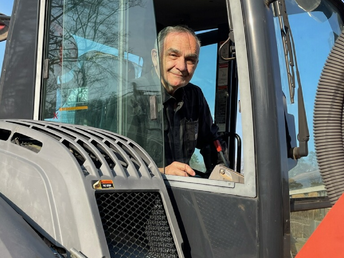 Dr. Kurti standing beside his excavator, a favorite tool for outdoor projects when he is not creating smiles at Kurti Orthodontics.